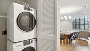 Een moderne wasruimte met gestapelde voorladers wasmachines en drogers, een eethoek met een houten tafel en stoelen, en grote ramen met uitzicht op de stad.