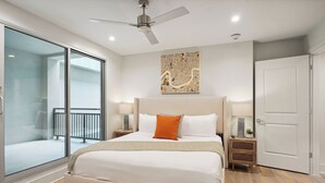 A modern hotel room with a large bed, a ceiling fan, a cityscape artwork, a sliding glass door, and a wooden floor. - The Eleanor 5BD/4B w Two Balconies, 8th Floor (New Orleans)