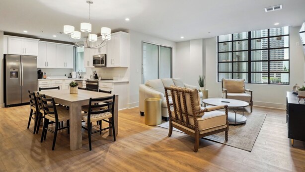 A modern kitchen with white cabinets, a stainless steel refrigerator, and a dining area with a wooden table and chairs. - The Eleanor 5BD/4B w Two Balconies, 8th Floor (New Orleans)