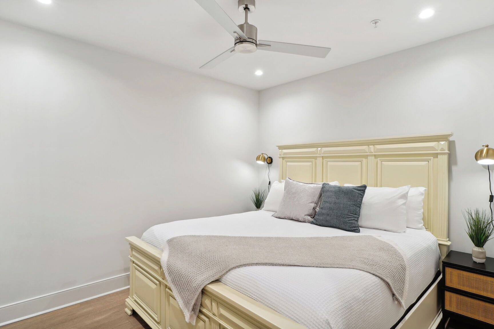 Une chambre à coucher comprenant un lit, des tables de chevet, un ventilateur de plafond et une lampe fixée au mur.