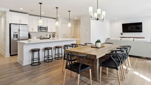 A modern kitchen with white cabinets, a stainless steel refrigerator, and a wooden dining table with black chairs. - The Eleanor 6BD/4B - Sleeps 16 (New Orleans)
