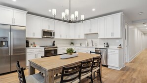 A modern kitchen with white cabinets, a stainless steel refrigerator, a microwave, and a wooden dining table with chairs.