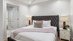 A bedroom with a tufted headboard, a bed with white linens, two bedside tables with lamps, a nightstand with a plant, and a ceiling fan.