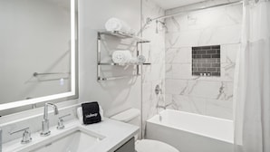 A modern bathroom with a large mirror, a sink with three faucets, a black towel, and a shower area with a curtain. - The Eleanor New Orleans 5BD/4B - All King Bedrooms (New Orleans)