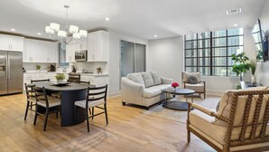 A modern kitchen with white cabinets, a dining table with chairs, a sofa, and a TV mounted on the wall. - The Eleanor 5BD/4B with Two Balconies (New Orleans)