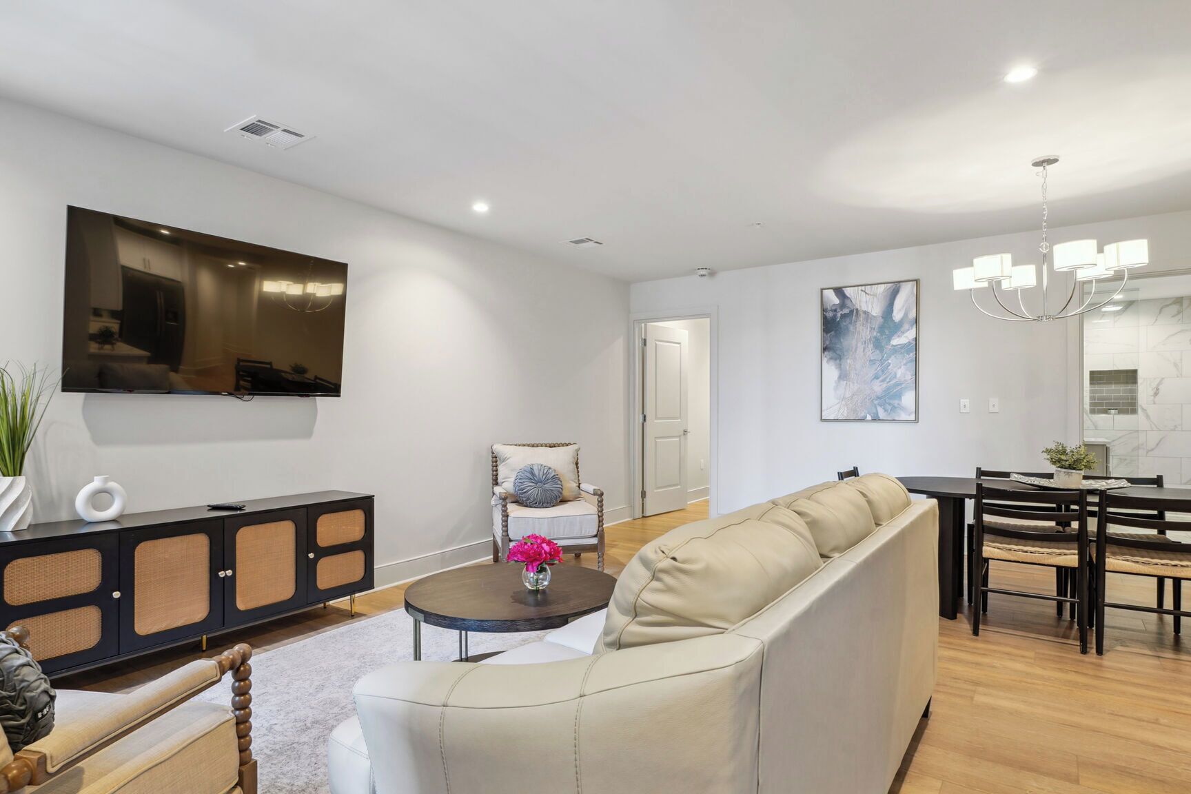 A modern living room with a sofa, a dining table, and a TV mounted on the wall.