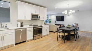 A modern kitchen with white cabinets, stainless steel appliances, and a dining area with a black table and chairs. - The Eleanor 5BD/4B with Two Balconies (New Orleans)