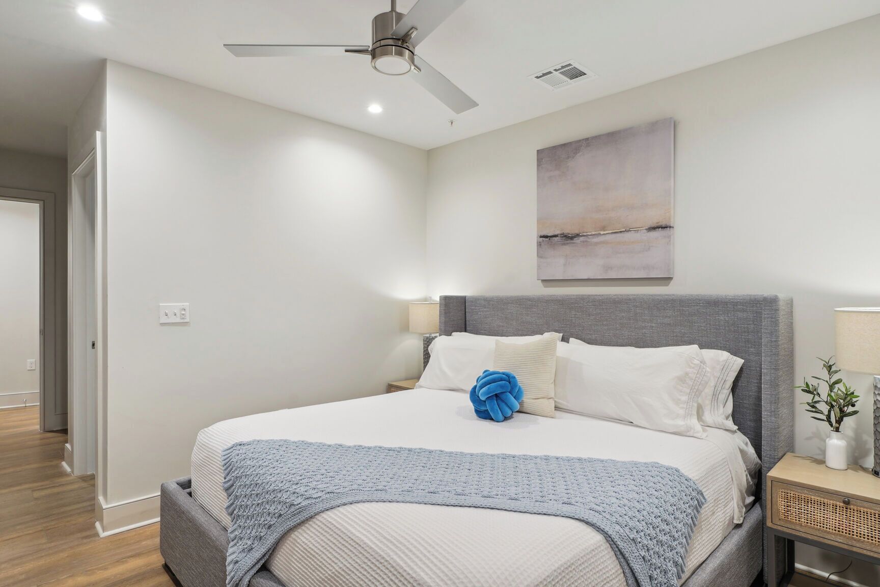 A modern bedroom with a bed, a ceiling fan, a nightstand, and a wall-mounted lamp.
