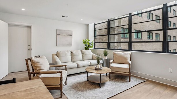 Un salon moderne comprenant un ensemble de canapés, deux fauteuils, une table basse et une grande fenêtre donnant sur un immeuble en briques.
