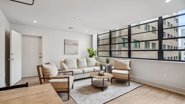 A modern living room with a sofa, two armchairs, a coffee table, and a large window with a city view. - The Eleanor 10BD/10B, All King Bedrooms w Ensuites (New Orleans)