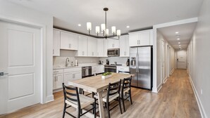 A modern kitchen with white cabinets, a stainless steel refrigerator, a wooden dining table with four chairs, and a pendant light fixture. - The Eleanor 10BD/10B, All King Bedrooms w Ensuites (New Orleans)