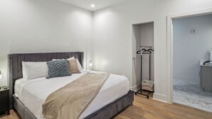 A modern bedroom with a bed, bedside tables, a ceiling fan, and a walk-in closet with a mirror and hanging clothes rack.