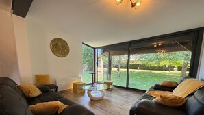 Ein modernes Wohnzimmer mit zwei schwarzen Ledersofas, einem Glastisch und einem großen Fenster mit Blick auf einen Garten.