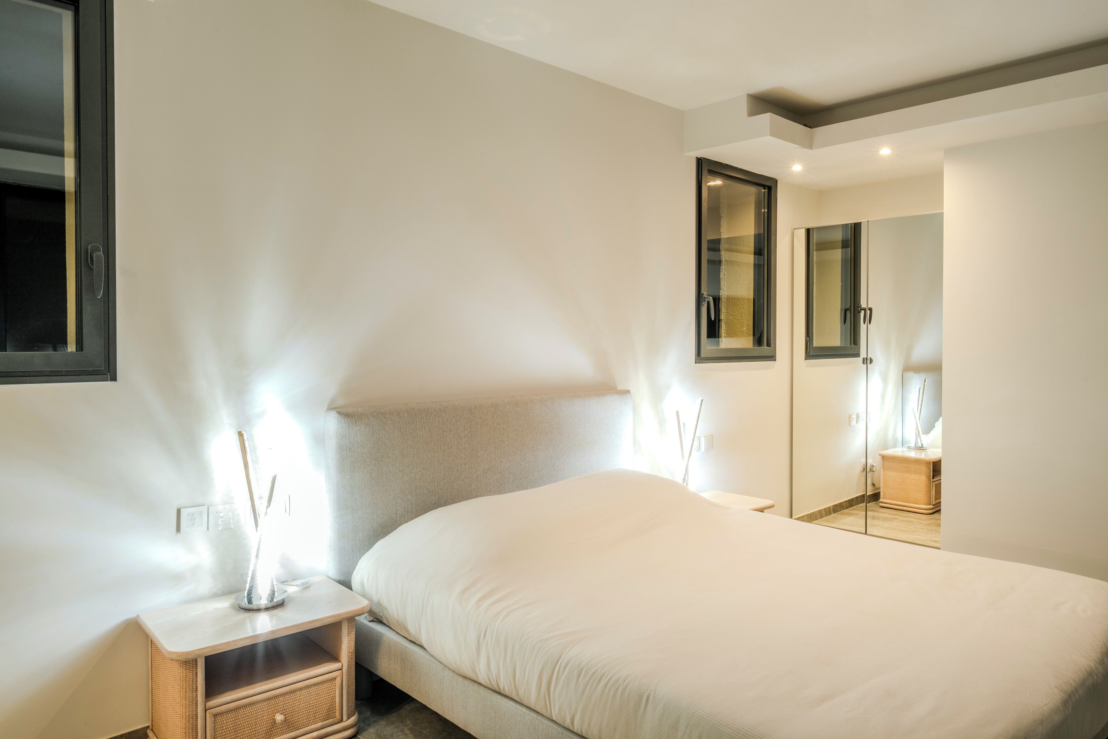 A modern hotel room with a large bed, bedside tables, a mirror, and a view of the hallway.