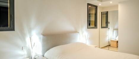 A modern hotel room with a large bed, bedside tables, a mirror, and a view of the hallway.