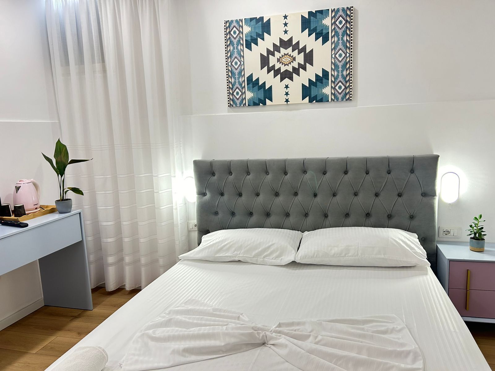 A neatly arranged bedroom with a tufted headboard, a bedside table with a lamp, and a wall-mounted artwork.