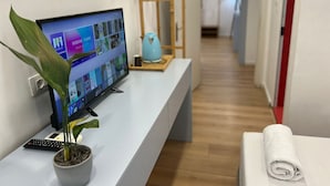 A reception desk with a computer monitor displaying a virtual meeting interface, a potted plant, a keyboard, and a rolled towel. - Tirana Square Hotel (Tirana)