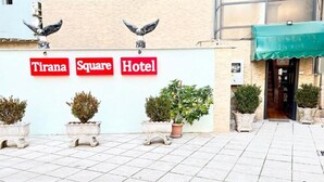 A hotel entrance with a sign reading "Tirana Square Hotel," potted plants, and a tiled pavement. - Tirana Square Hotel (Tirana)