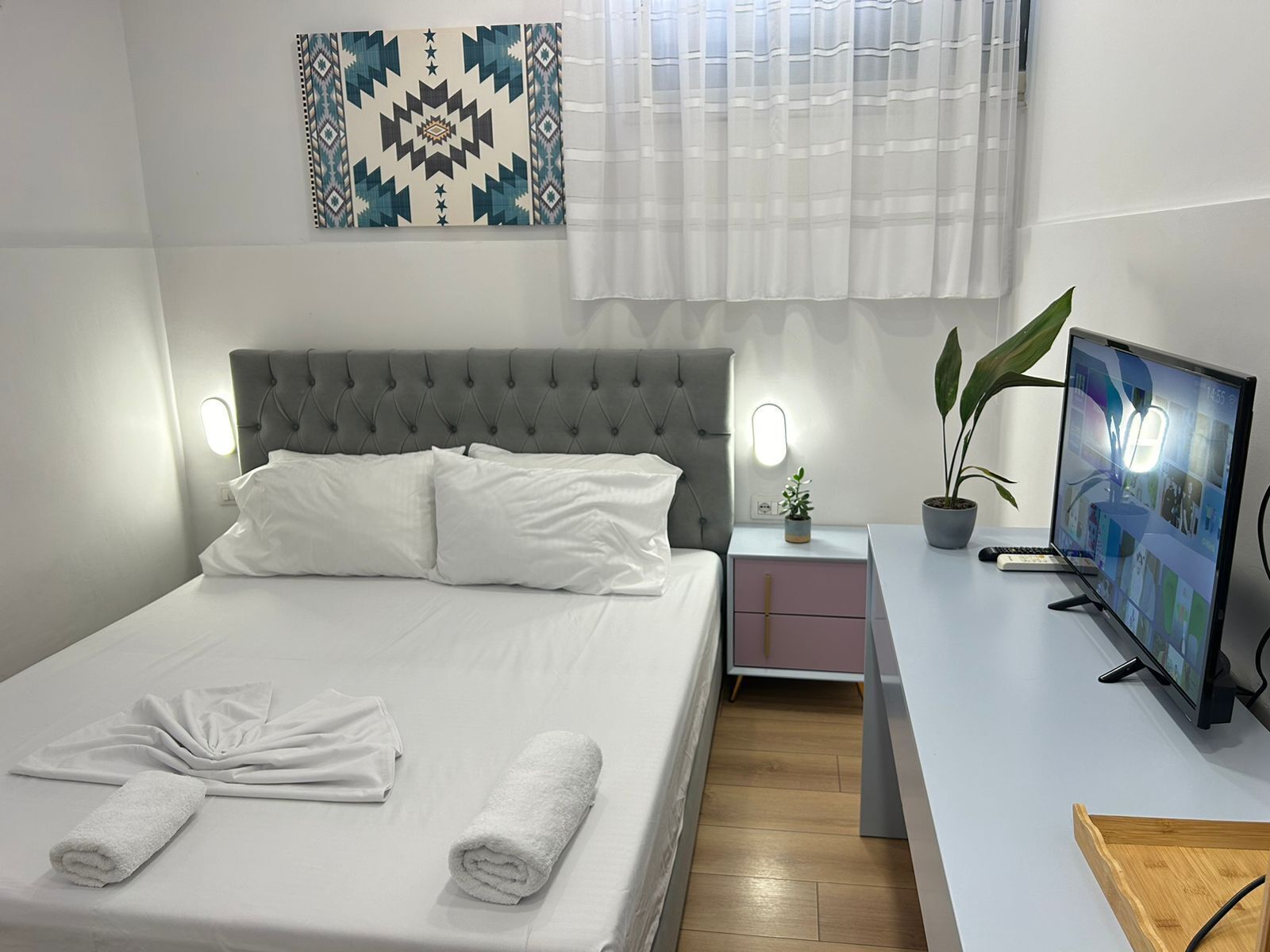 A modern bedroom with a large bed, bedside tables, a TV, and a decorative wall piece.