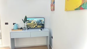 A modern room with a white desk, a flat-screen TV, a kettle, and a potted plant. - Tirana Square Hotel (Tirana)