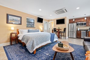 Ein Hotelzimmer mit Bett, Schreibtisch, Stuhl, einer Küchenzeile inklusive Kühlschrank und Mikrowelle sowie einem an der Wand montierten Fernseher.