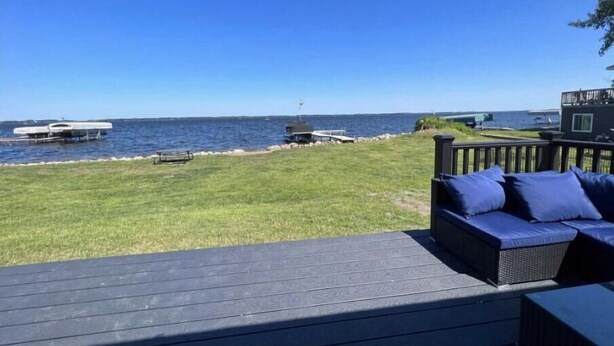 A deck with a view of the sea, a grassy area, and a small boat docked.