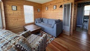 A cozy cabin interior with a grey sofa, patterned cushions, a small wooden table, and wooden walls.