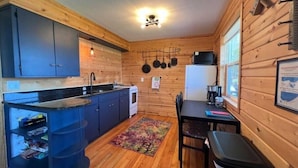 A compact kitchen with wooden walls, a small dining area, and a refrigerator.