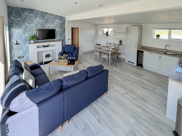 A modern living room with a sectional sofa, a flat-screen TV, a fireplace, and a dining area with a table and chairs.