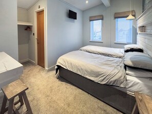 Un dormitorio con dos camas, una puerta de madera, un televisor en la pared y una ventana con persianas.