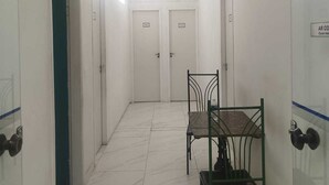 Um corredor com piso de azulejos, duas portas com a inscrição '100' e uma mesa com cadeiras.