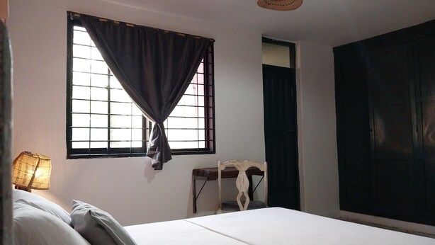 Una habitación con cama, cortinas en la ventana, una lámpara y un armario.