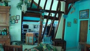 Ein gemütliches Wohnzimmer mit einem Korbssessel, einem Holzesstisch und einer Küchenzeile im Hintergrund.