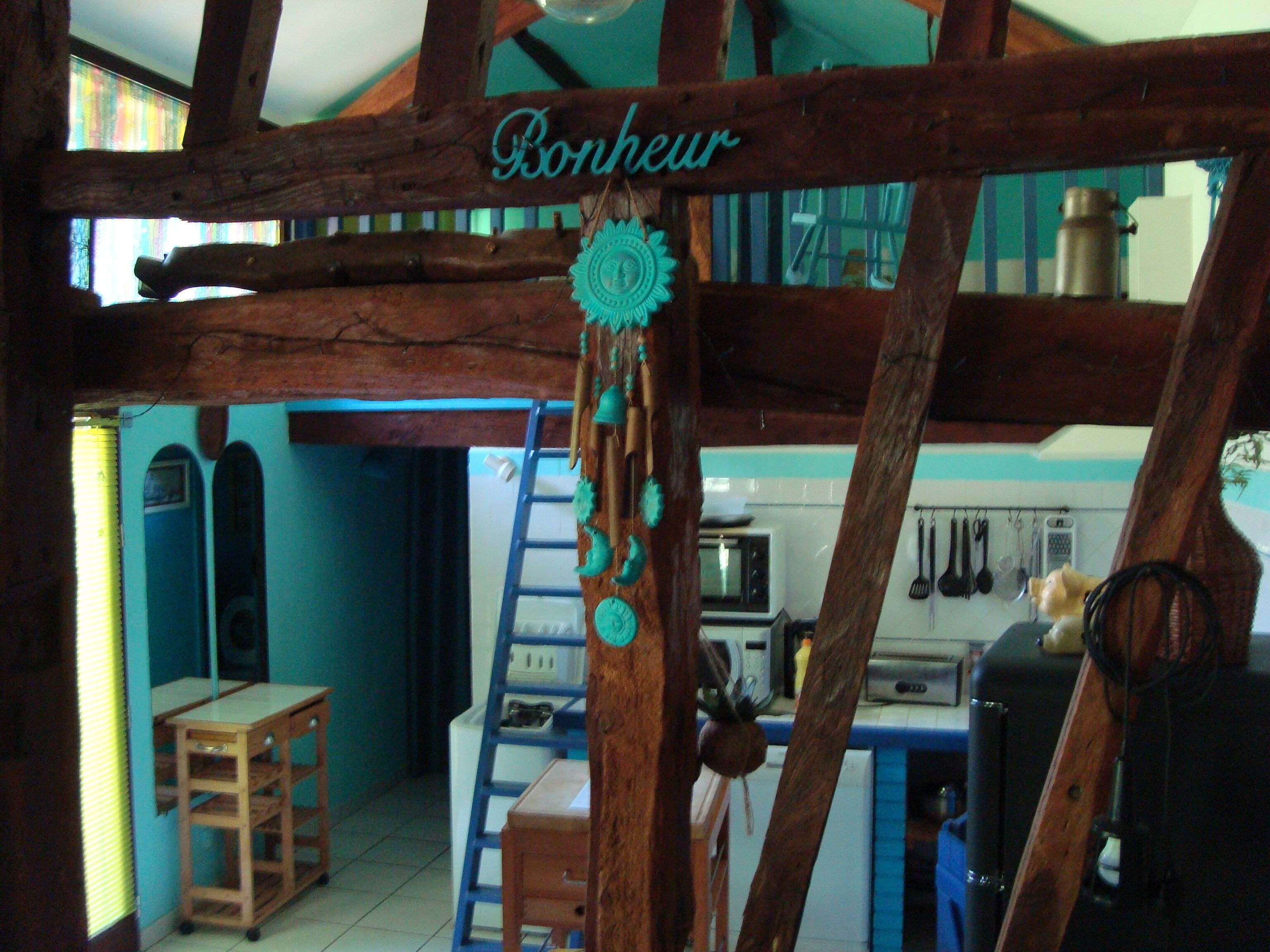 A rustic kitchen with wooden beams, a wooden table, a ladder, and a kitchen counter with various utensils.