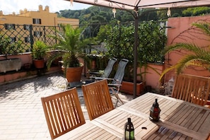 A wooden table and chairs under a pergola with potted plants and a view of buildings and trees. -  Attic for 2 with wonderful private terrace in Trastevere  (Roma)