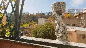 Un balcon agrémenté d’un vase décoratif, d’une treille et offrant une vue sur les bâtiments et les arbres.