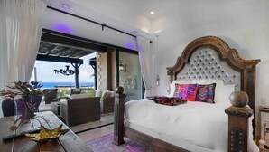 Une chambre avec un grand lit, une vue sur l’océan et un balcon aménagé avec du mobilier d’extérieur.