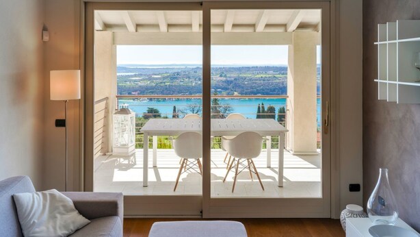 A room with a sliding glass door leading to an outdoor terrace with a table and chairs, a sofa, and a lamp. - WOW what a view! Charming apartment with terrace, pool and fitness center (Salo')
