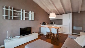 A modern living room with a flat-screen TV, a white console, and a dining area with chairs. - WOW what a view! Charming apartment with terrace, pool and fitness center (Salo')