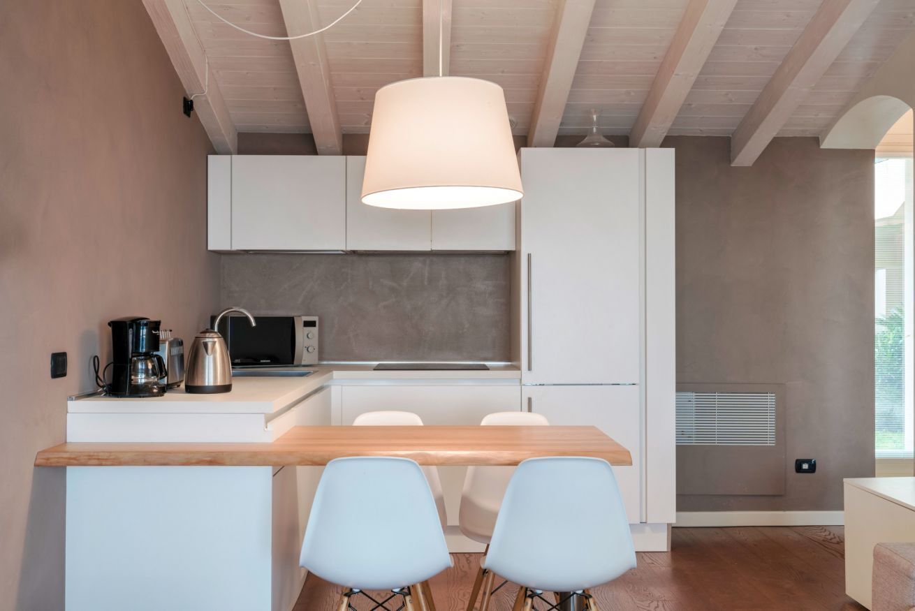 Una cocina moderna con armarios blancos, encimera de madera y lámpara colgante.