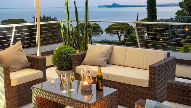 A balcony with wicker furniture, a glass table, and a view of the sea.