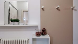 A bathroom with a white radiator, a mirror, a shelf with plants and a cup, and two glass jars with brown contents.