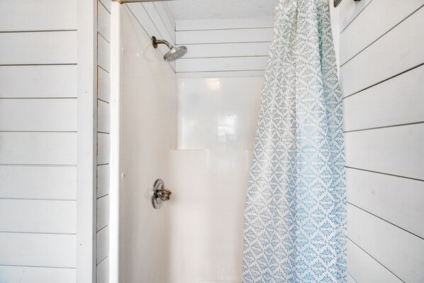 A shower with a patterned curtain and a handheld showerhead.