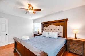 Un dormitorio con cama de madera, ventilador de techo, mesita de noche con lámpara y ventana con persianas.