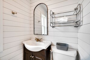Un baño con lavamanos blanco, mueble de madera oscura, un espejo y un perchero de cromo.