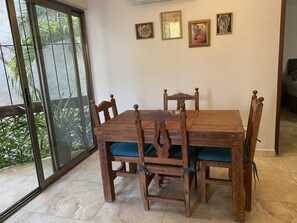 Enjoy meals in this dining area with a wooden table and four comfortable chairs, surrounded by framed artworks and a sliding door leading to an outdoor space.