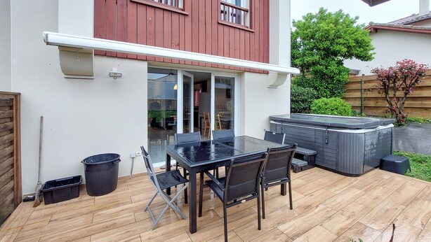 A patio with a glass table and chairs, a hot tub, and a wooden deck.