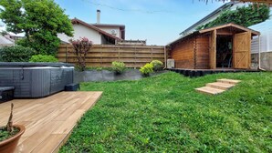 A backyard with a wooden deck, a hot tub, a wooden shed, and a garden area with various plants and flowers.