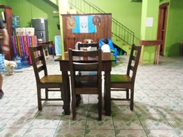 Un comedor con una mesa y sillas de madera, un dispensador de agua y una escalera al fondo.