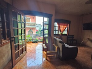 An open doorway leading to a balcony with potted plants, a cushioned bench, and a television on the wall. - Hosteria del Centro (Santiago Atitlán)